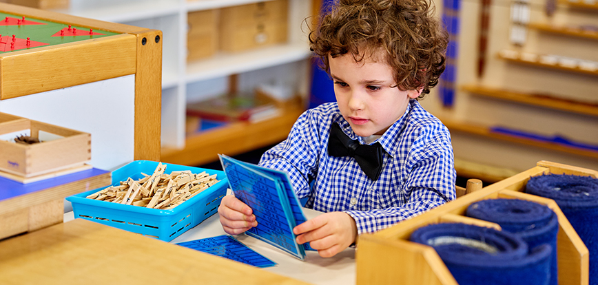 Jonge leerling zit aan een tafel in de klas met een montessori-werkje