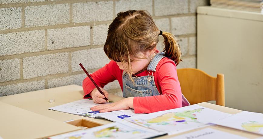 Een jonge montessori-leerling zit aan haar tafel in de klas en oefent het schrijven