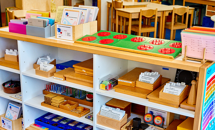 Een kast met vakken, waarin en waarop allerlei montessori-werkjes en montessori-materialen liggen