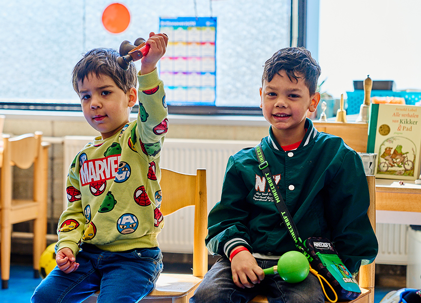Twee montessori-leerlingen zitten op stoeltjes in de kring en hebben allebei een muziekinstrument in de hand