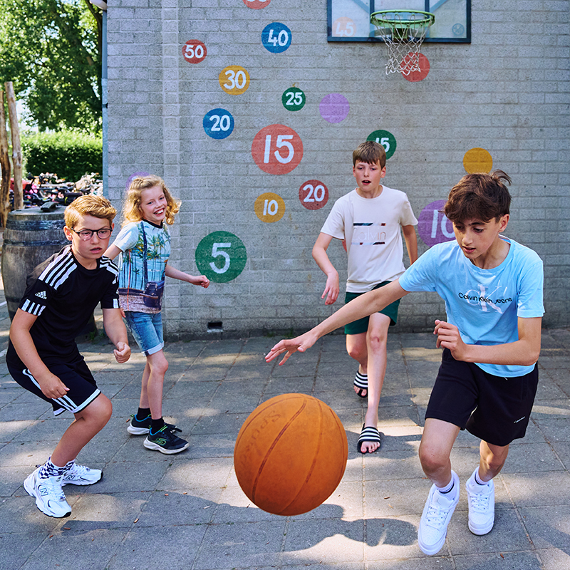 Een groepje jongens speelt basketbal op het schoolplein.