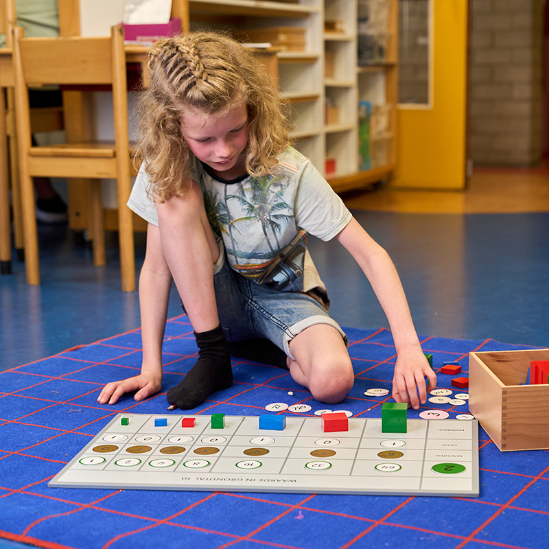 Een leerling werkt op een kleedje op de grond in de klas.