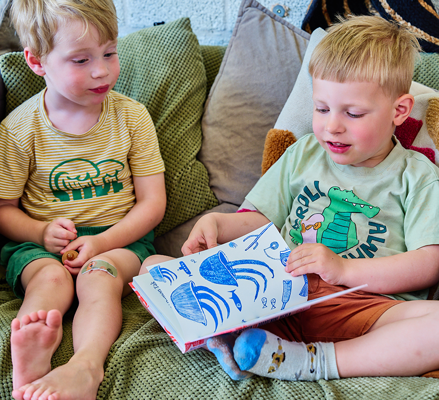 Twee peuters zitten op een bankje en lezen een boek.