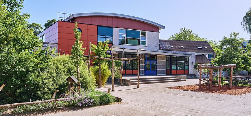 Een sschoolplein met veel groene struiken en natuurlijke speeltoestellen.