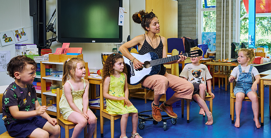 Vakdocent met een gitaar zingt samen met de leerlingen van de onderbouw.