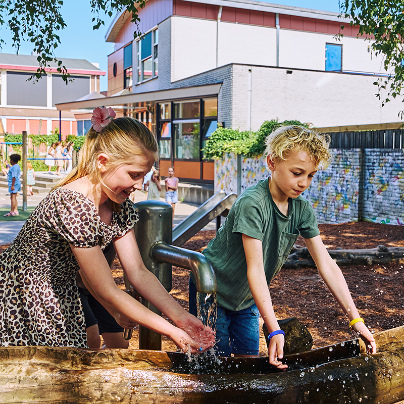 Twee leerlingen spelen enthousiast met water op het schoolplein.